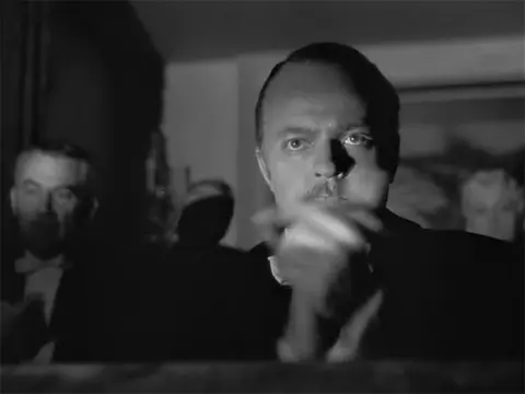 Citizen Kane, animated: Charles Foster Kane, in black and white, applauding slowly and deliberately in a crowded room.